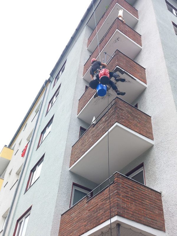 Two technicians rappelling past balconies for facade repair
