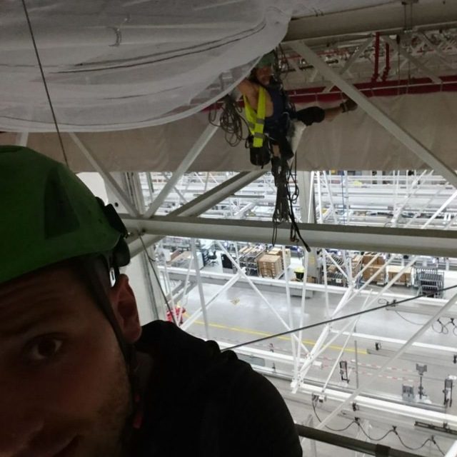 Rigging technicians working overhead trusses inside a logistics facility